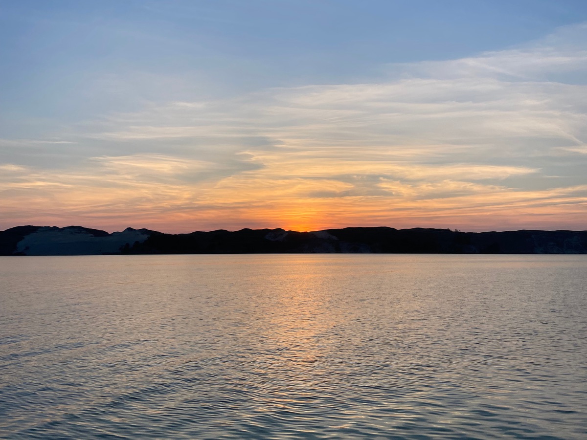 Saulėlydis virš marių, kopų siluetas horizonte.
